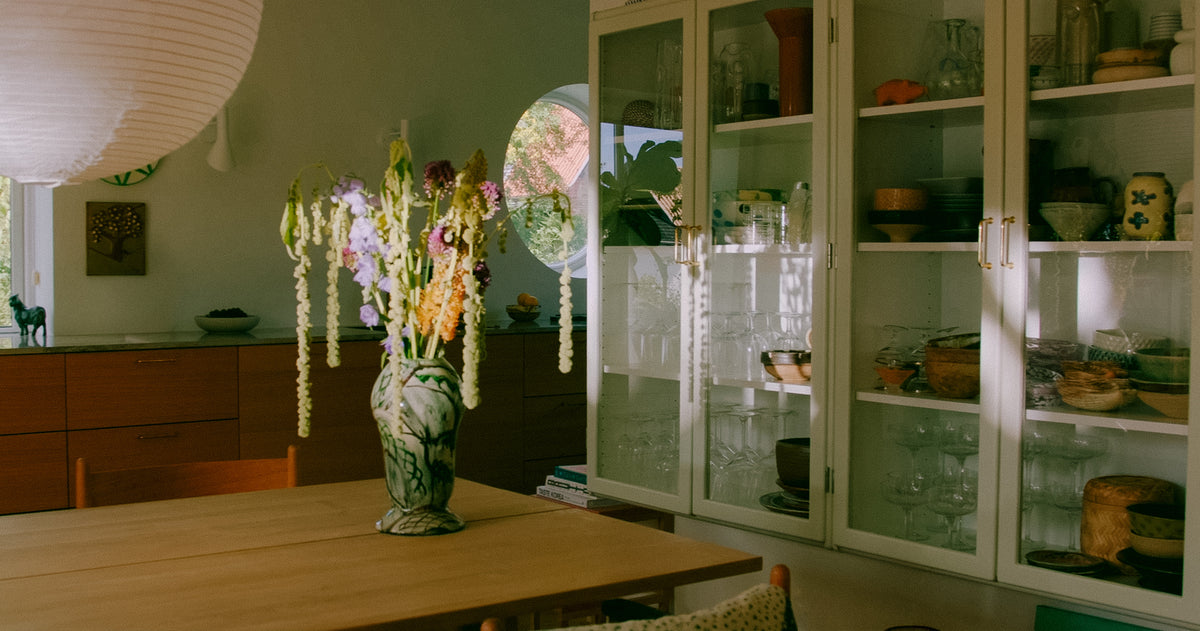 Spisebord med blomstervase foran hvid glasvitrine med glas og keramik